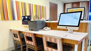 Et hotelreceptionsskrank med to Apple iMac computere, en skrivebordstelefon og en check-in kiosk. Der er tre stribede stole med polstrede sæder. Gulvet har et mønstret tæppe.