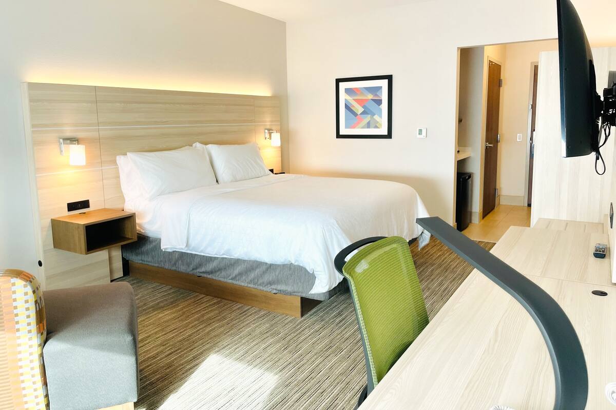 Habitación de hotel con cama, mesitas de noche, un escritorio, una silla, un televisor de pantalla plana y un cuadro en la pared.