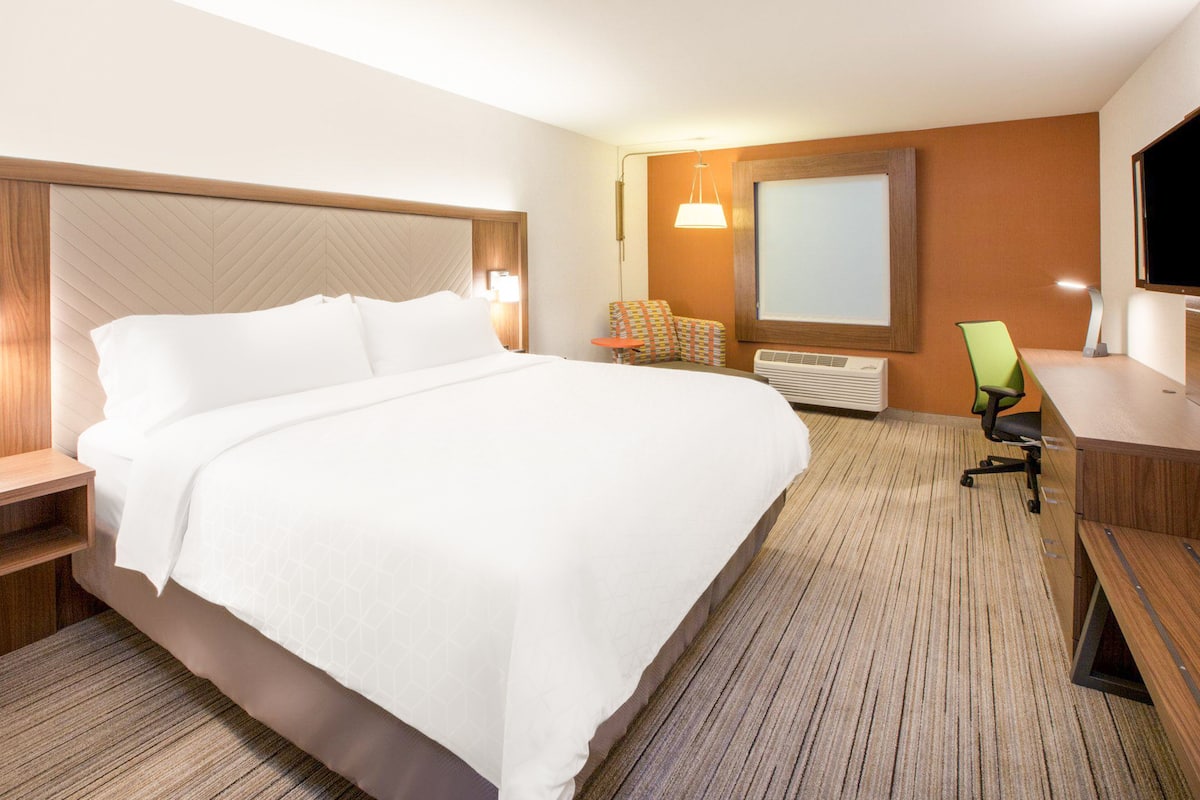 Una habitación de hotel con una cama grande, un escritorio, una silla, un televisor y una ventana.