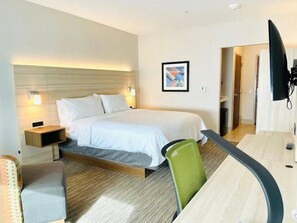 A hotel room with a bed, bedside tables, a desk, a chair, and a television.