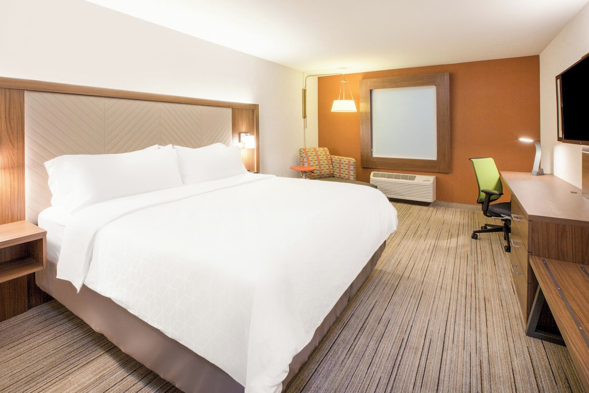 A hotel room with a large bed, a desk, a chair, a television, and a window.