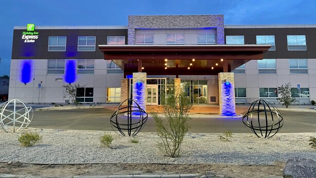 En Holiday Inn Express & Suites bygning med moderne design, der har en overdækket indgang og dekorativ belysning.