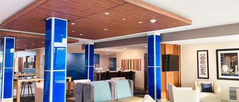 Una hall d'albergo moderna con soffitto in legno, dettagli blu, un'area salotto con divani e poltrone, una zona pranzo e opere d'arte alle pareti.