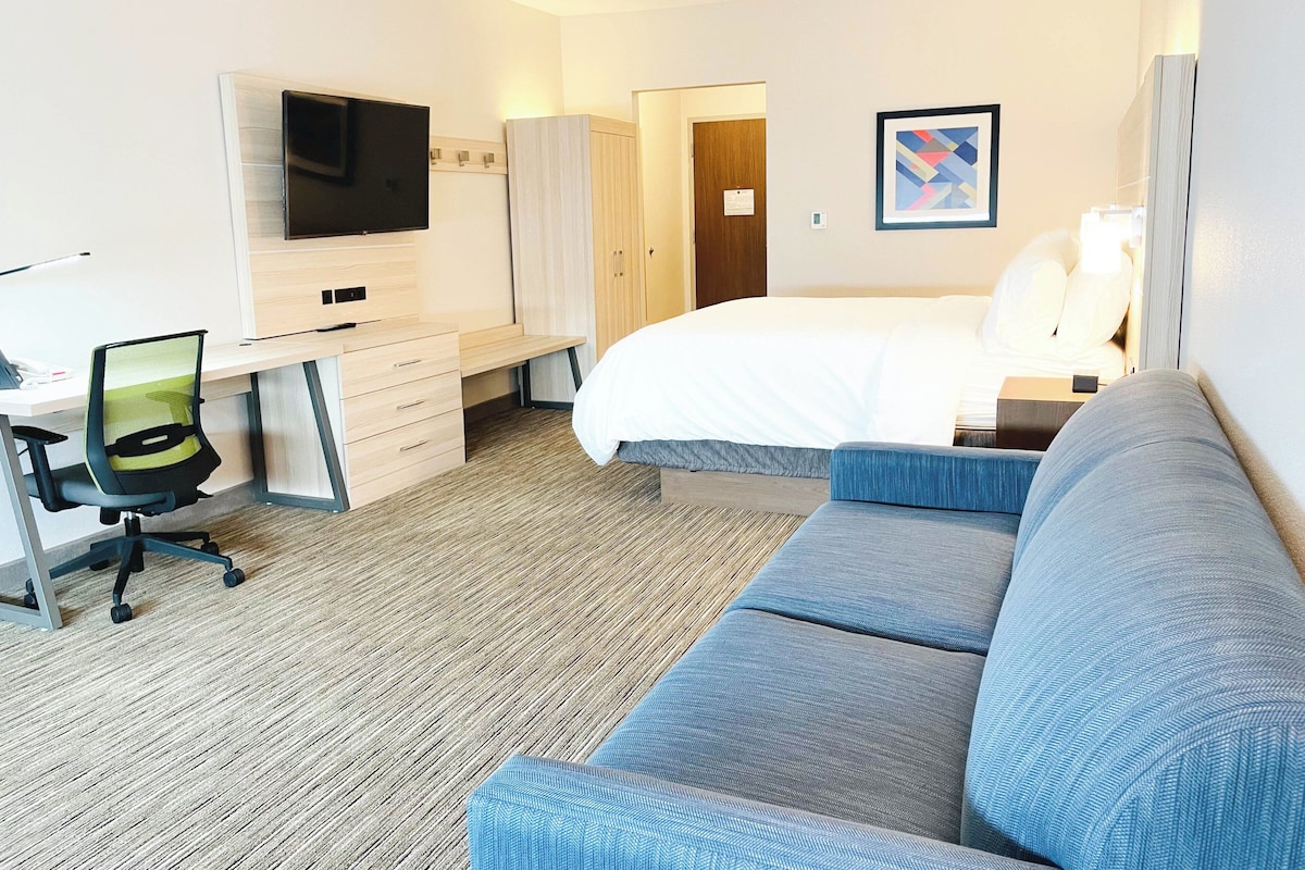 A hotel room with a bed, a desk with a chair, a television, a wardrobe, and a painting on the wall.