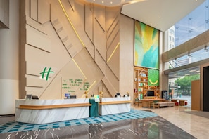 A modern hotel reception area with a marble reception desk, multilingual welcome sign, and a large window offering a view of the city. - Holiday Inn Shanghai Nanjing Road by IHG (Shanghai)