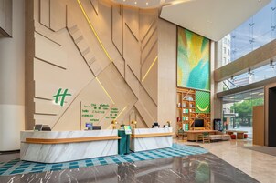 A modern hotel reception area with a marble reception desk, multilingual welcome sign, and a large window offering a view of the city.