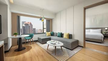 A modern hotel room with a large window, a sofa, a dining table, and a bed.