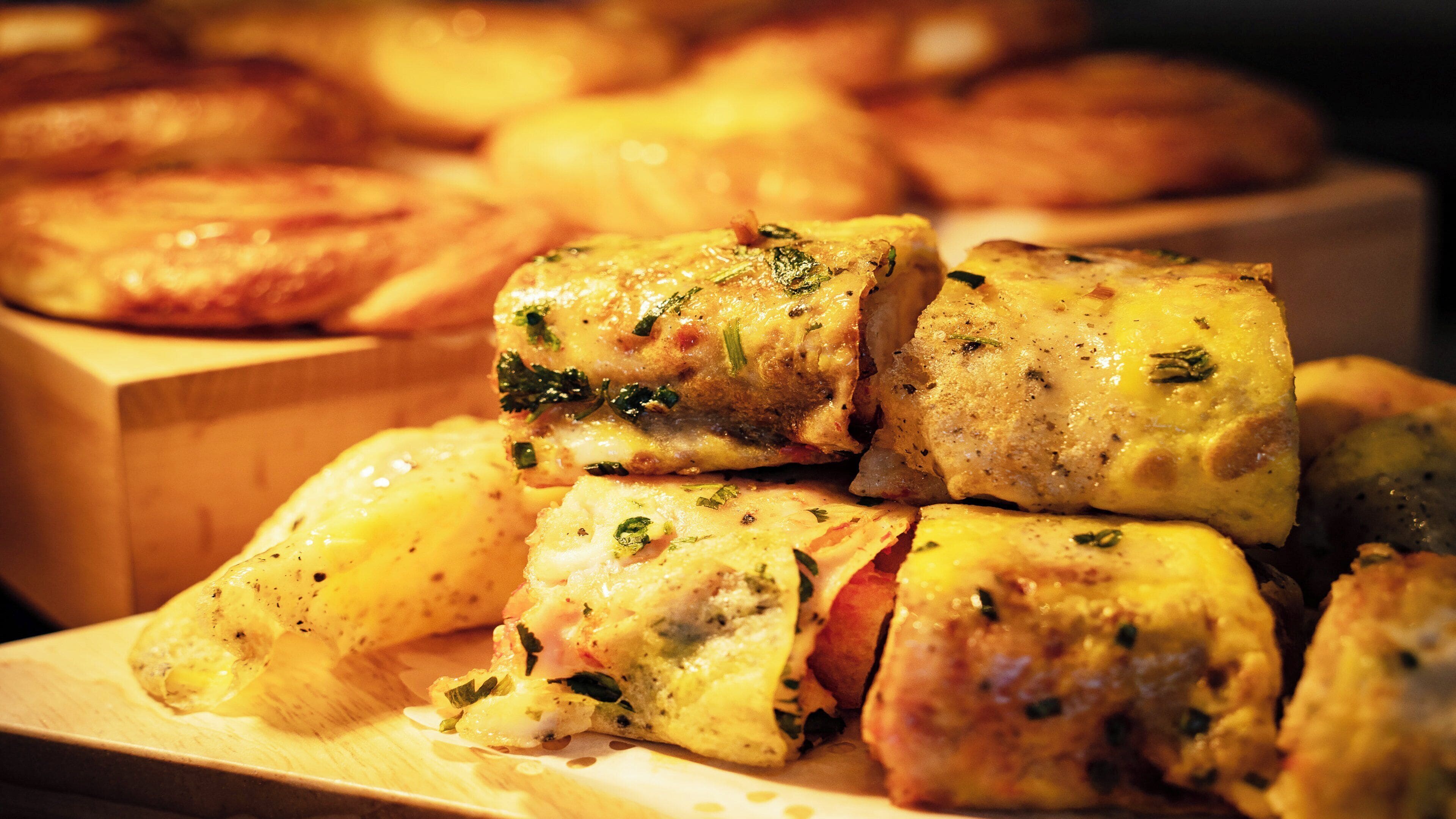 A wooden cutting board with several pieces of food, possibly a dish with herbs and cheese.