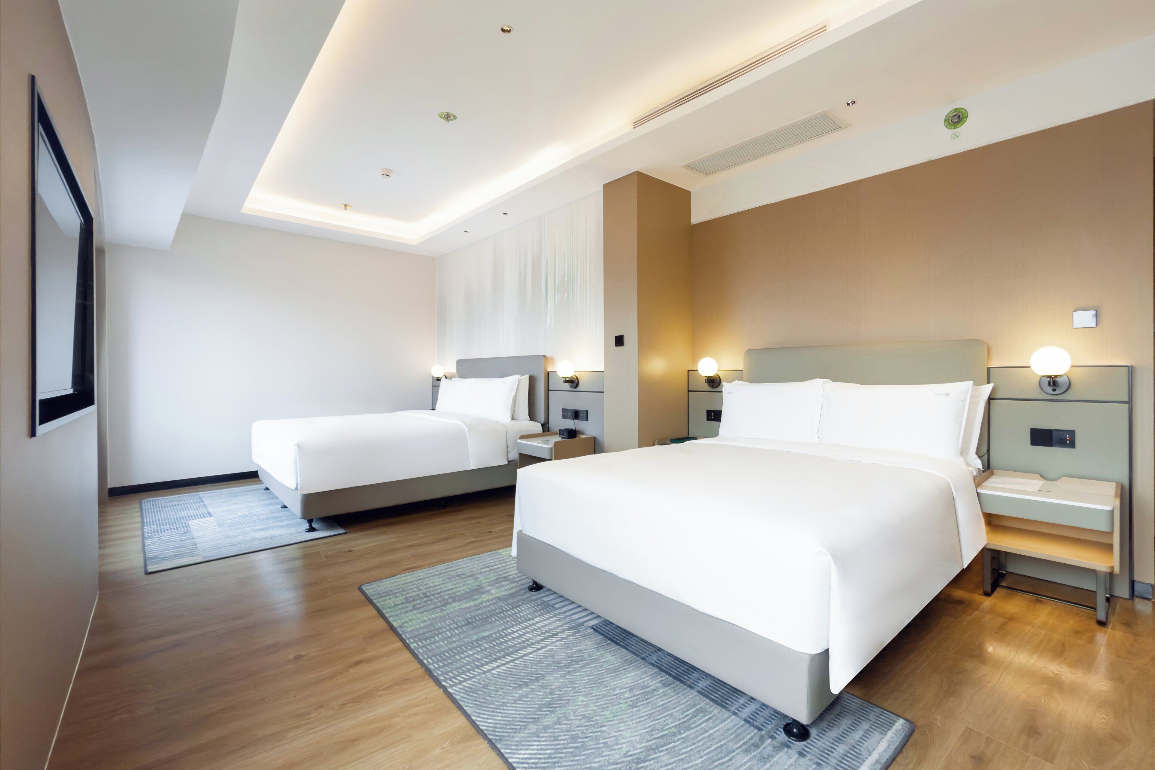 A modern hotel room with two beds, a large mirror, and a wooden floor.