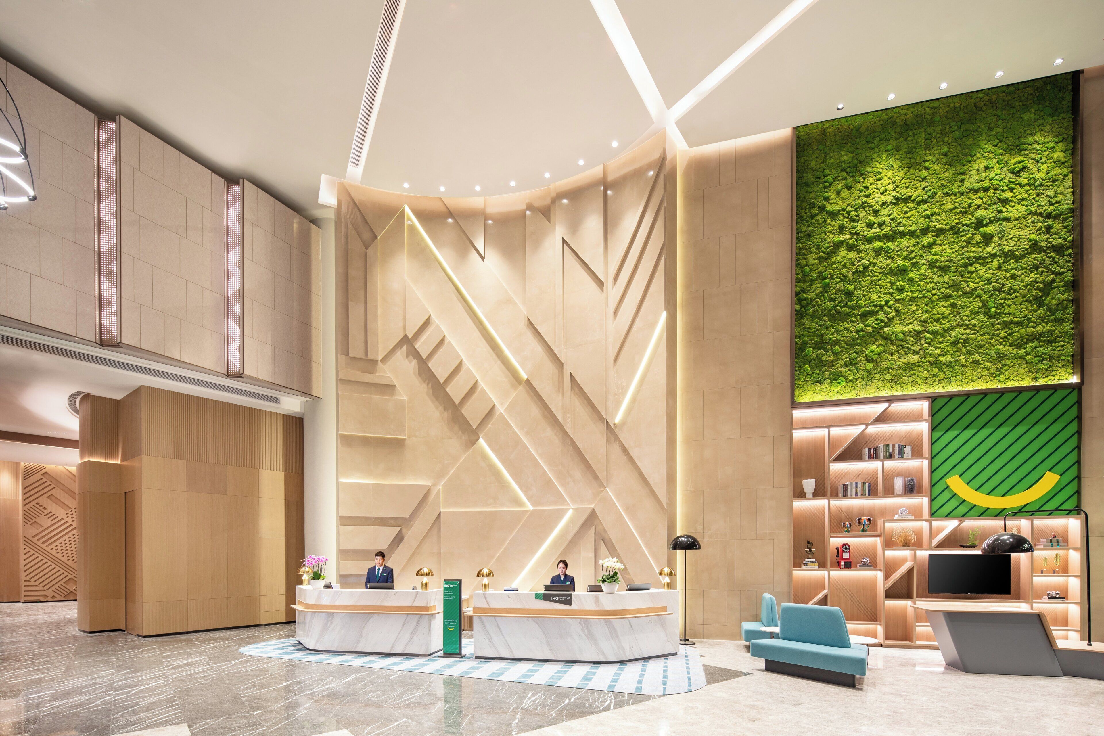 A modern lobby with a reception desk, seating area, and a green vertical garden wall.