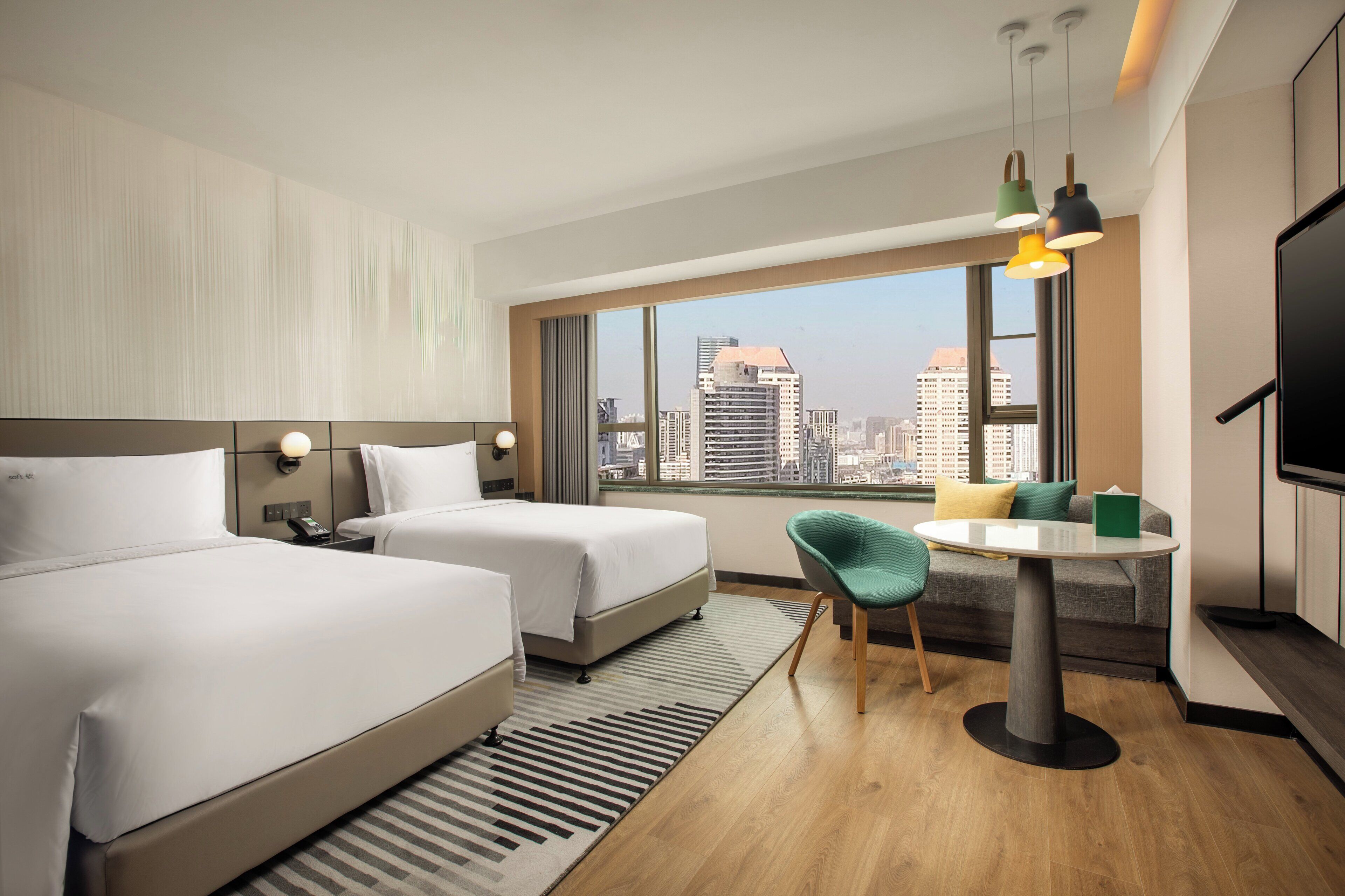 A hotel room with two beds, a desk, a chair, a TV, and a large window with a city view.