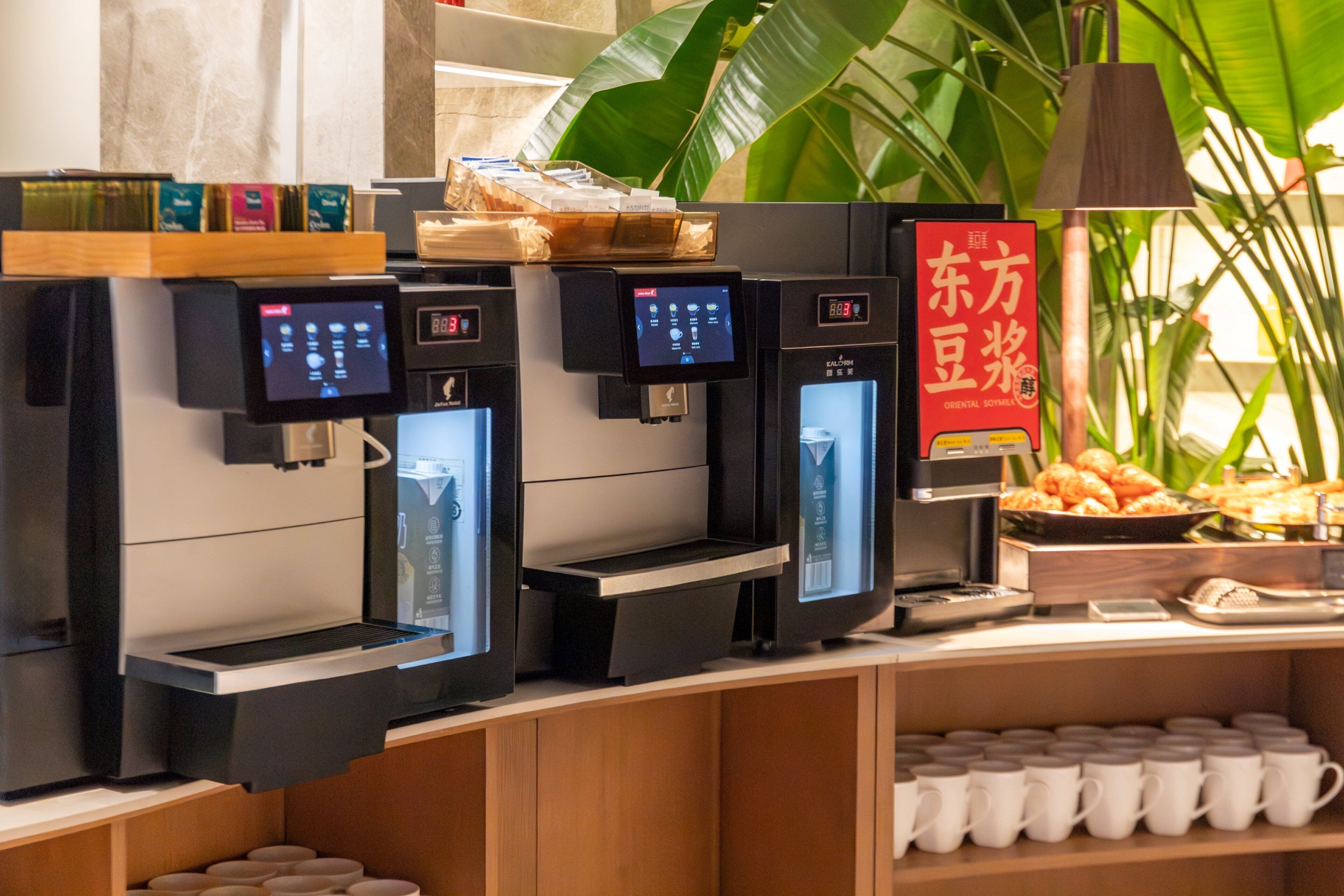A coffee station with multiple espresso machines, a sign for Oriental Soymilk, and a display of pastries.