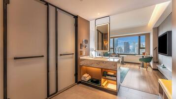 Un moderno baño de hotel con puerta corredera, tocador con espejo y vistas a la ciudad a través de la ventana.