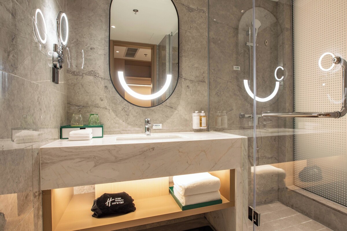 A modern bathroom with a marble vanity, a glass shower enclosure, and a towel rack.