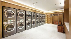 A row of front-loading washing machines in a well-lit, modern laundry facility with wooden paneling and storage baskets. - Holiday Inn Shanghai Nanjing Road by IHG (Shanghai)