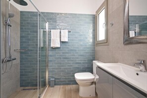 Ein modernes Badezimmer mit einer Duschkabine, einer weißen Toilette und einem großen Waschbecken mit Spiegel.