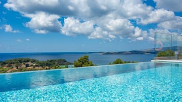 Un ciel d’un bleu limpide parsemé de nuages, une piscine à l’eau claire et une vue sur la mer et la terre au loin.