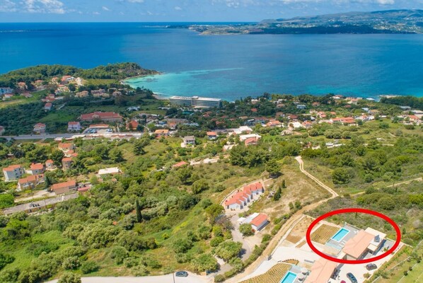 Ett flygbildsbild av ett bostadsområde vid kusten med hus, ett stort hotell och en pool.