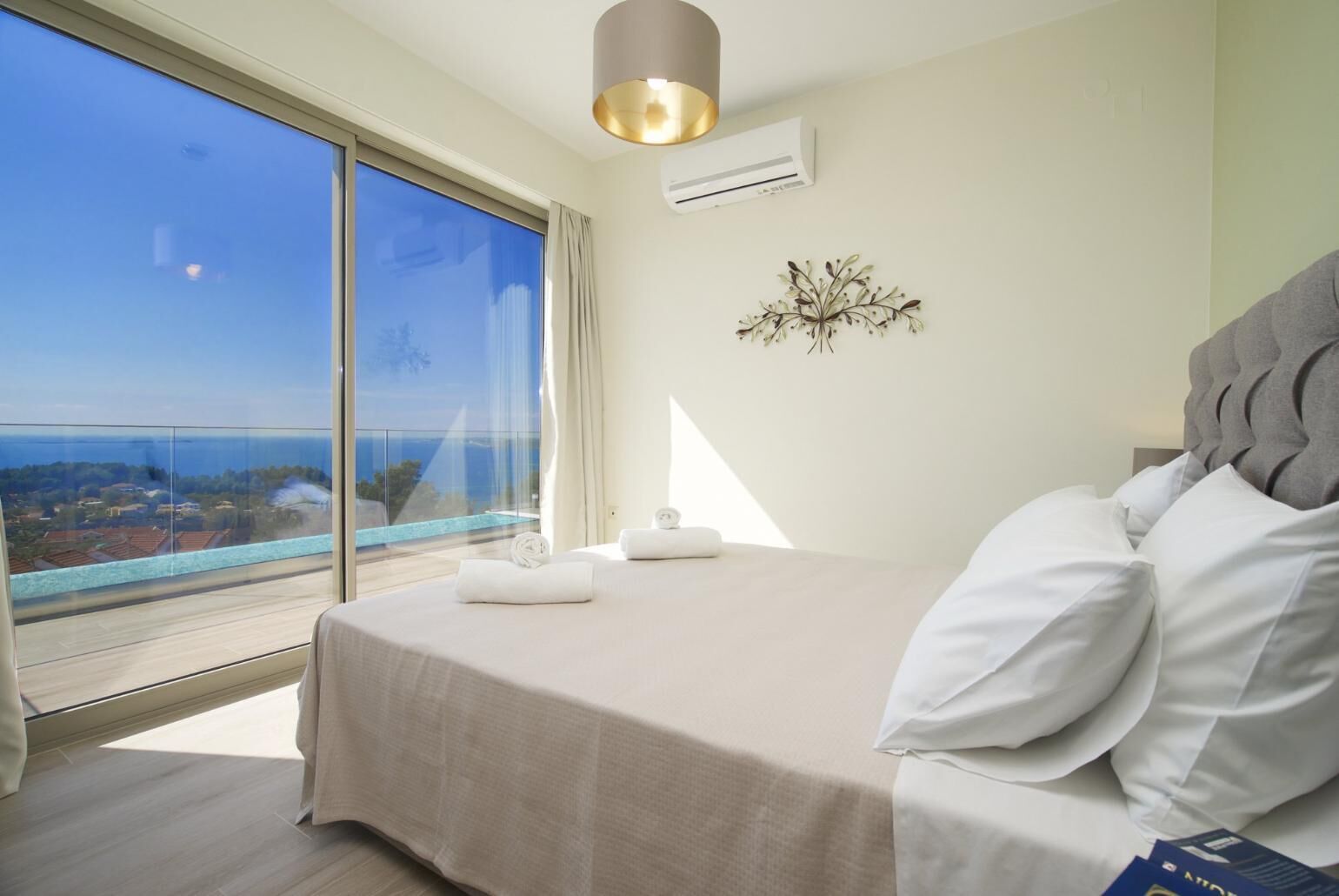 Une chambre avec un grand lit, une vue sur la mer, un luminaire au plafond et un climatiseur fixé au mur.