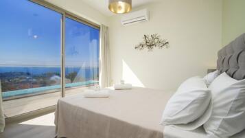 Une chambre avec un grand lit, une vue sur la mer, un luminaire au plafond et un climatiseur fixé au mur.