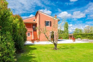 Una casa de dos pisos con fachada roja, un porche delantero y un jardín cuidado.