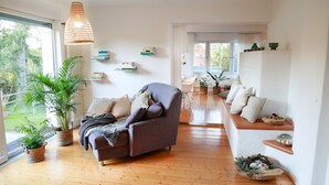 Ein modernes Wohnzimmer mit einer Couch, Topfpflanzen und einem Essbereich mit einer Bank.