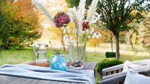 Ein Holztisch mit einer klaren Glasgießkanne, einer blauen Vase und einer Vase mit Blumen.
