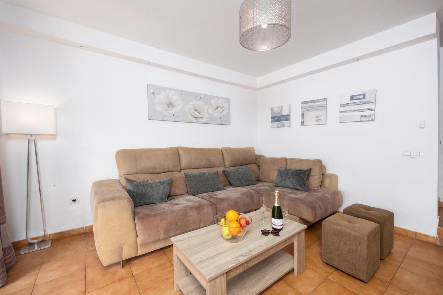 A living room with a beige sofa, a wooden coffee table with fruits and glasses, and a lamp.