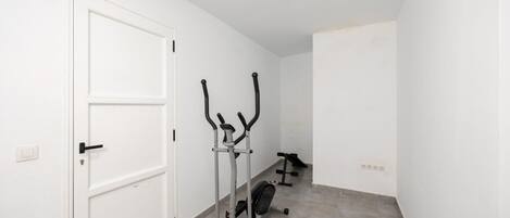 Un pasillo con una puerta blanca, dos bicicletas estáticas y una cinta de correr.