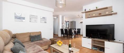 Un salon moderne avec un canapé, un téléviseur et un coin repas à l’arrière-plan.