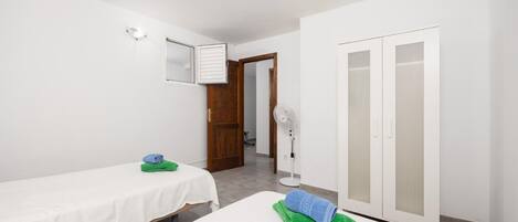 A bedroom with two single beds, a wardrobe, a fan, and a door leading to another room.