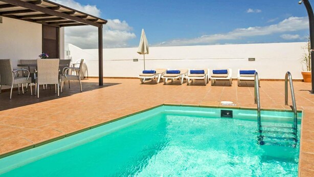 A rooftop pool with a clear view of the sky, a covered seating area with chairs, and a poolside bar.