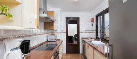 A modern kitchen with white cabinets, a stainless steel range hood, a built-in oven, a coffee maker, and a refrigerator.