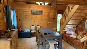 A wooden cabin interior with a dining table, chairs, a sofa, and a staircase.