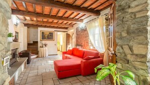 Una sala de estar acogedora con un sofá rojo, paredes de piedra, una chimenea y una escalera que conduce a otra habitación.