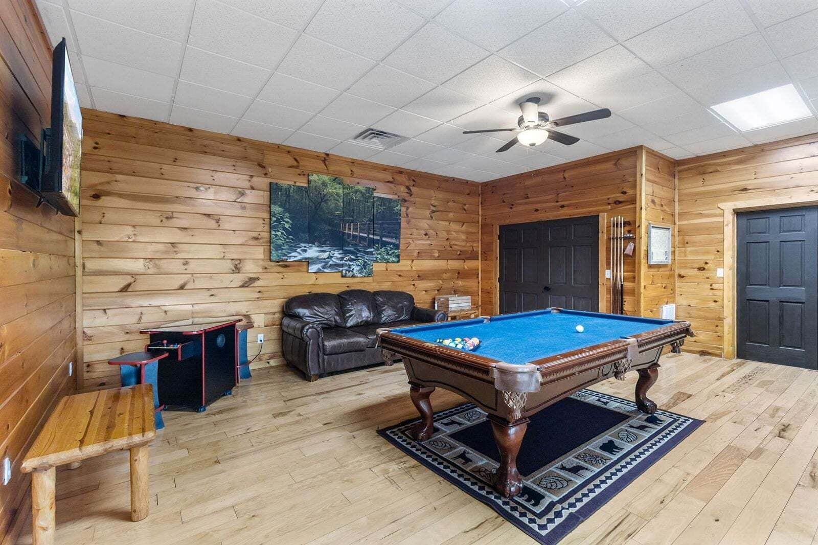 Una habitación con paneles de madera, una mesa de billar, un sofá de cuero, un televisor y un ventilador de techo.