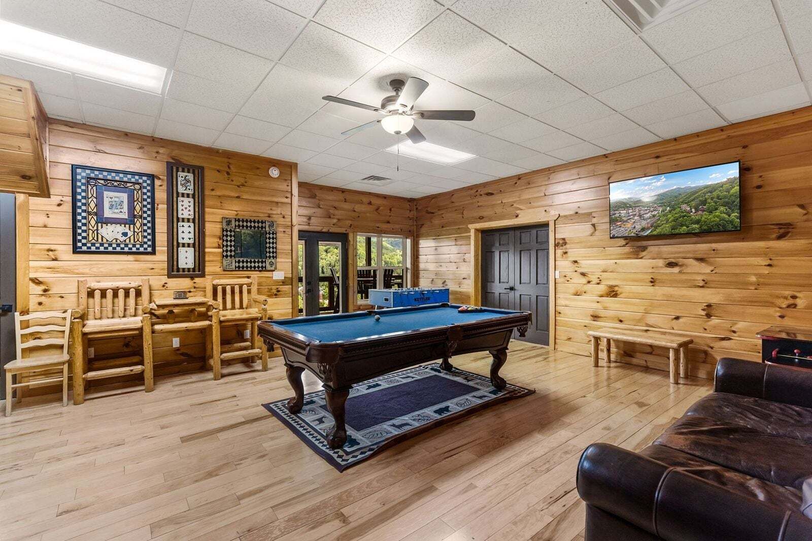 A wooden interior with a pool table, chairs, a sofa, and a television.