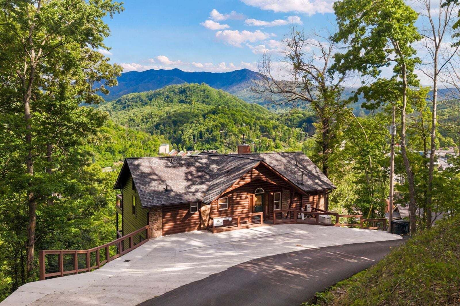 A log cabin with a porch, surrounded by trees and mountains.