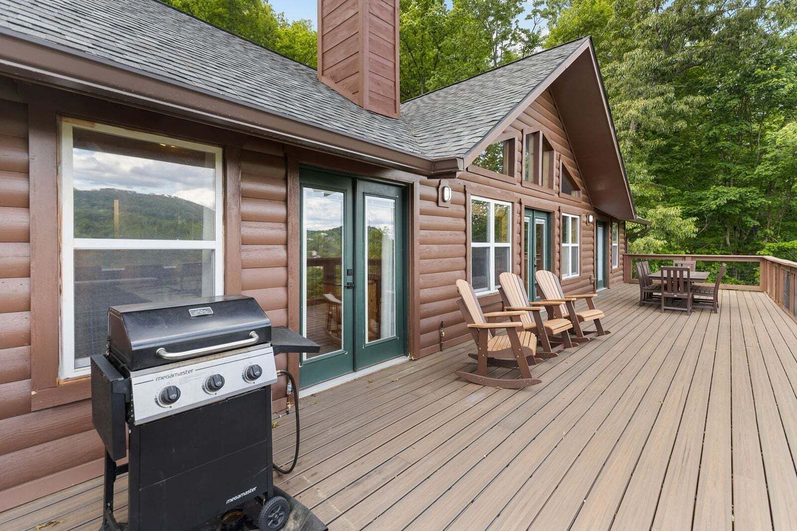 Una cabaña de madera con terraza, una parrilla y asientos al aire libre.