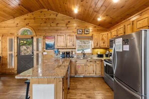 A wooden cabin-style kitchen with a granite countertop, stainless steel appliances, and wooden cabinets.
