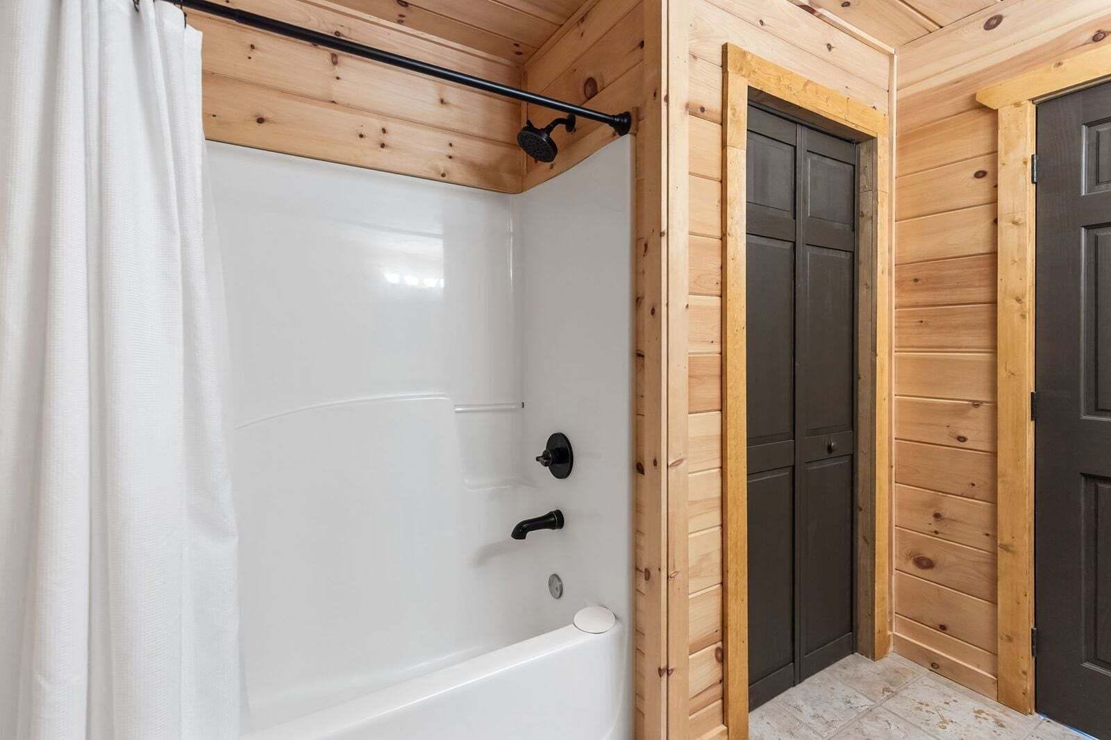 A wooden cabin bathroom with a white bathtub, a showerhead, and a door.