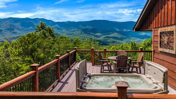 Una terraza de madera con un jacuzzi, sillas y una mesa, con vistas a un paisaje montañoso.