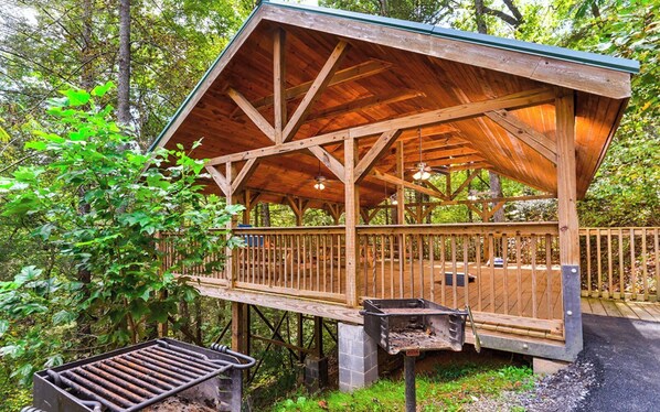 Uma cabana de madeira com varanda, churrasqueira e base de pedra.