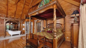 A four-poster bed with a canopy, a clawfoot bathtub, and a wooden chair in a log cabin bedroom.