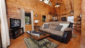 A cozy wooden cabin interior with a living room featuring a sofa, a coffee table, a television, and a fireplace.
