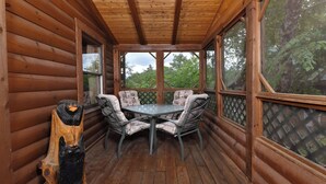 A wooden deck with a table and chairs, surrounded by wooden walls and large windows.