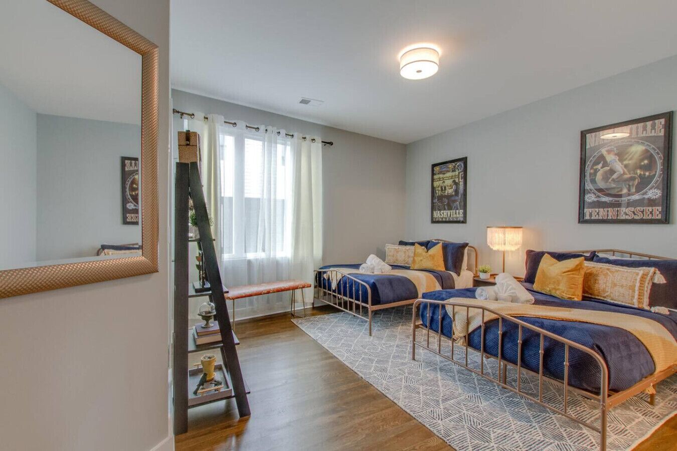 Une chambre avec deux lits, un grand miroir, une échelle et une fenêtre avec des rideaux.