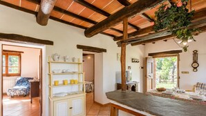 A rustic kitchen with a wooden table, shelves with kitchenware, and a view to the outside. - Villa Bellavista Large Private Pool, WiFi (Ortignano Raggiolo)