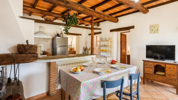 A dining area with a table set for four, a kitchen in the background, and a television on a wooden cabinet. - Villa Bellavista Large Private Pool, WiFi (Ortignano Raggiolo)