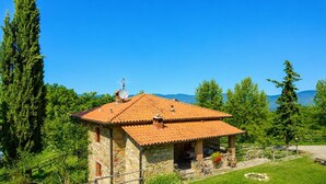 A stone house with a tiled roof, surrounded by greenery and mountains in the background. - Villa Bellavista Large Private Pool, WiFi (Ortignano Raggiolo)